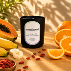 Candle labeled 'multifaceted' with fruits and a plant on a wooden surface