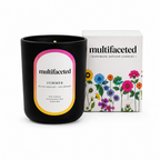 Black candle with 'multifaceted' label and floral packaging on a white background